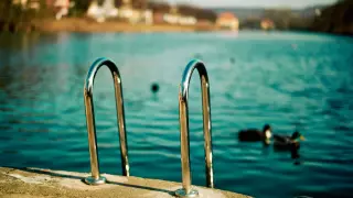 Im Zentrum eine Trittleiter aus verchromtem Stahl die vom betonierten, bräunlich schimmernden Steg aus zum blaugrünlich wirkenden Wasser des Neckars herunterreicht.