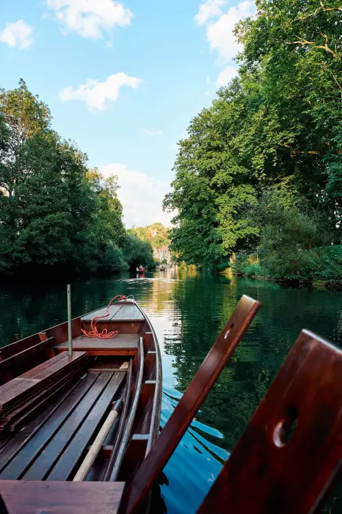 Blick von einem aus braunem, lackierten Holz gefertigten Stocherkahn auf den von grünen Bäumen am Ufer gesäumten Fluss Richtung Tübinger Neckarfront im September.