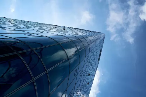 Bürohochhaus, welches in schräger Perspektive vom linken, unteren Bildrand nach rechts zur Mitte verläuft und (mich) an die "Battlestar Galactica" erinnert. Die komplett verglaste Oberfläche spiegelt den blauen, fast wolkenlosen Himmel an einem sonnigen Junitag.