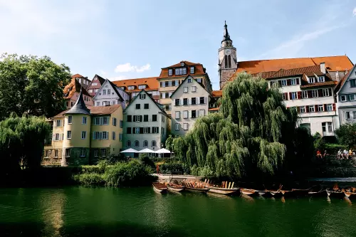 Blick vom Neckar auf den Hölderlinturm, einige davor vertäute Stocherkähne, Teile der sogenannten Neckarfront  und die Stiftskirche im Hintergrund, an einem sonnigen Julitag.