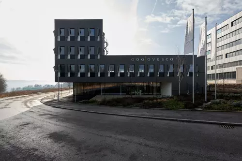 Frontansicht vom Firmengebäude in Tübingen. Auffällig sind die rechteckigen Fenster, vertikal ausgerichtet beziehungsweise deren „Fensterläden“ (die keine sind). Diese sehen aus wie links anschlagende MetallSegel.