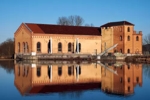 Historisches Wasserkraftwerk der Gemeinde Kiebingen, an einem sonnigen Wintertag, das sich auf der Wasseroberfläche des angestauten Neckars spiegelt.