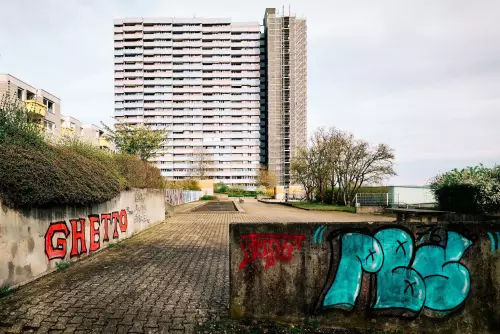 Hochhaus im Tübinger Stadtteil Waldhäuser-Ost mit 22 Stockwerken aus circa 200 Meter Entfernung. In Rot ist  das Wort "Ghetto" auf eine Betonmauer im nahen Vordergrund gesprüht worden.
