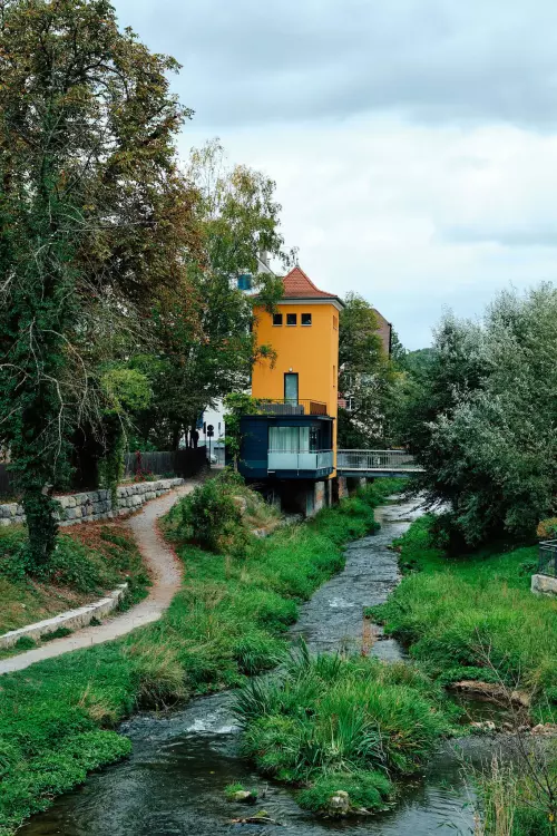 Ammerzonas - Die von Einheimischen liebevoll übertriebene Bezeichnung für die relativ kleine, renaturierte Ammer. Im Zentrum ein am Ufer stehender "Wohnturm" mit orangefarbener Fassade.