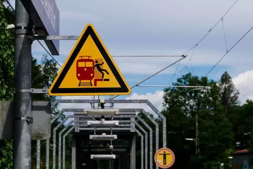 Warnschild vor der Gefahr zu nah am Eisenbahngleis zu stehen, während ein Zug im Bahnhof einfährt.