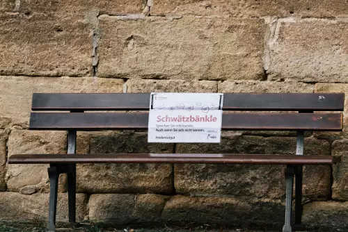 Holzbank vor der Jakobuskirche in Tübingen mit einem Schild und der Aufschrift: "Sprechen Sie miteinander. Auch wenn Sie sich nicht kennen."