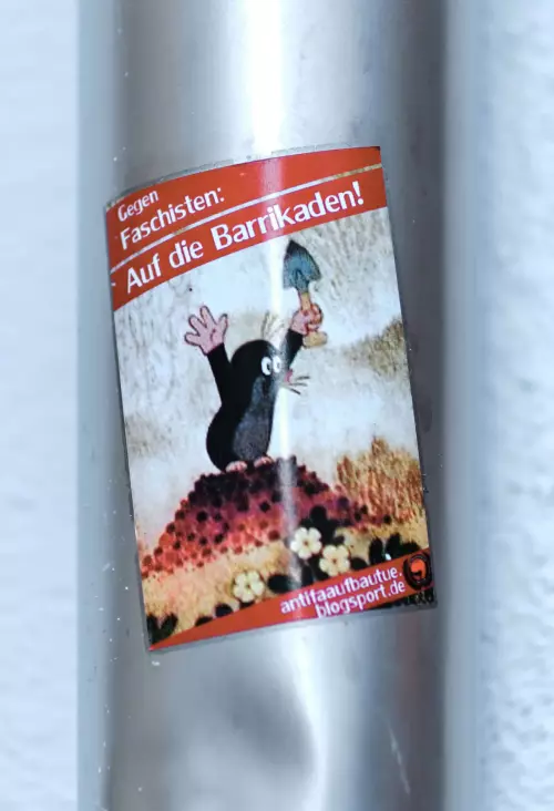 Aufkleber an einem Regenrohr; Der "kleine Maulwurf" steht mit einem Spaten in der Hand und nach oben ausgestreckten Armen auf seinem Maulwurfshügel. Darüber steht: "Gegen Faschisten: Auf die Barrikaden!" - Aktion einer AntiFa-Gruppe aus Tübingen.