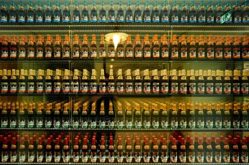 Fünf horizontal verlaufende Reihen übereinander gestellter Bierflaschen, die in einer beleuchteten Glasvitrine präsentiert werden.