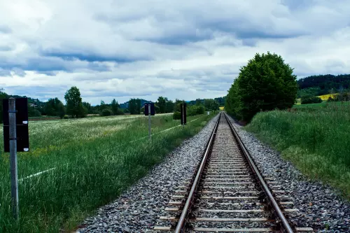 Eisenbahngleise der Ammertalbahn in Tübingen im grauen Gleisbett von grünen Bäumen und  Wiesen eingerahmt.