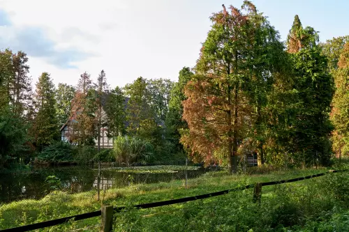 Kotten in Versmold Peckeloh, abseits der Straßen, umgeben von Laub- und Nadelbäumen an einem größeren Gartenteich gelegen.