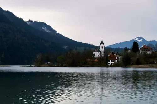 Blick über den Hopfensee, an einem grauen Novembertag, auf eine Kirche; Im Hintergrund die Berge.