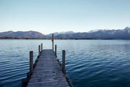 Bootssteg am Ufer vom Forggensee im Allgäu. Im Hintergrund das Alpenpanorama.