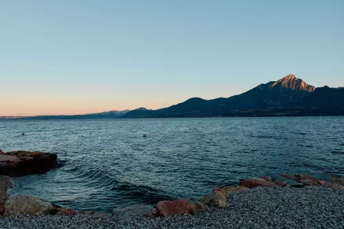 Gardasee, Ostufer, in der Nähe von Torri del Benaco, 5 Uhr Morgens. Erste Sonnenstrahlen erreichen die gegenüberliegenden Bergspitzen, wobei der höchste Gipfel der Monte Pizzocolo ist.
