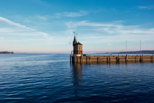 Blick vom Ufer Konstanz auf den Bodensee und das am Ende des Steegs stehende Fähr- oder Wachturmhäuschen(?) abseits der Imperia.