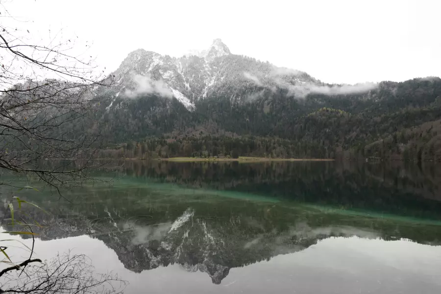 SOOC-Version - Blick vom Rundwanderweg Alpsee auf den am Gipfel leicht verschneiten Gassenthomaskopf, der sich in der grünlichen, ganz ruhigen Seeoberfläche spiegelt.