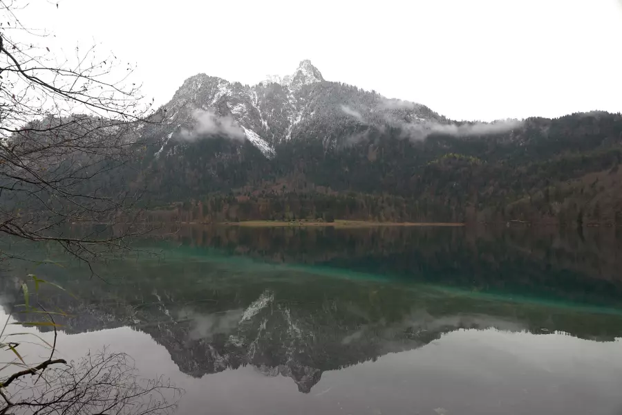 DNG-Version - Blick vom Rundwanderweg Alpsee auf den am Gipfel leicht verschneiten Gassenthomaskopf, der sich in der grünlichen, ganz ruhigen Seeoberfläche spiegelt.