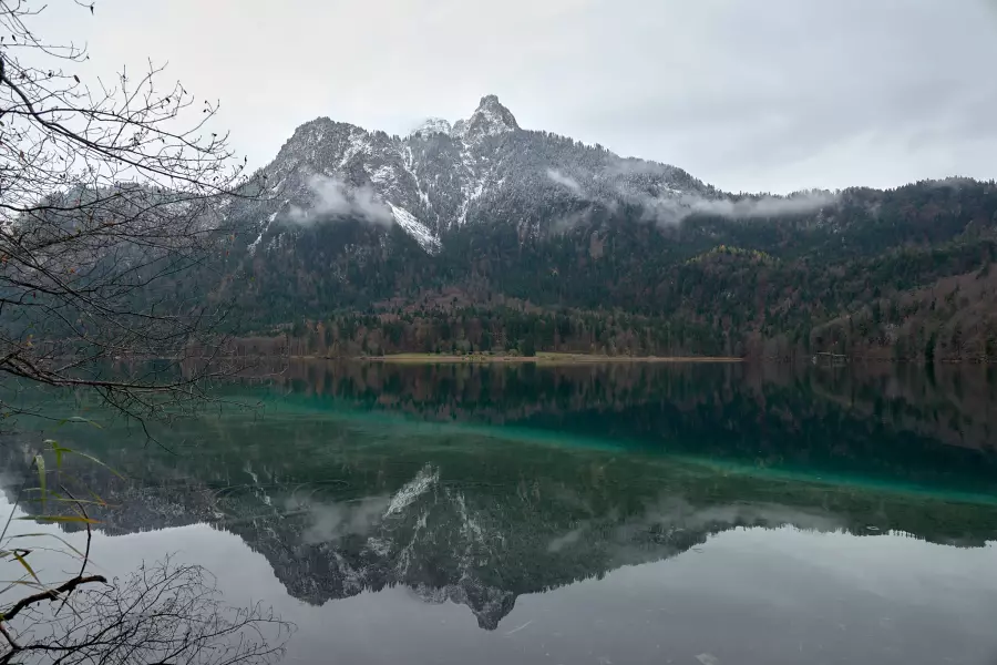 RAW-Version - Blick vom Rundwanderweg Alpsee auf den am Gipfel leicht verschneiten Gassenthomaskopf, der sich in der grünlichen, ganz ruhigen Seeoberfläche spiegelt.
