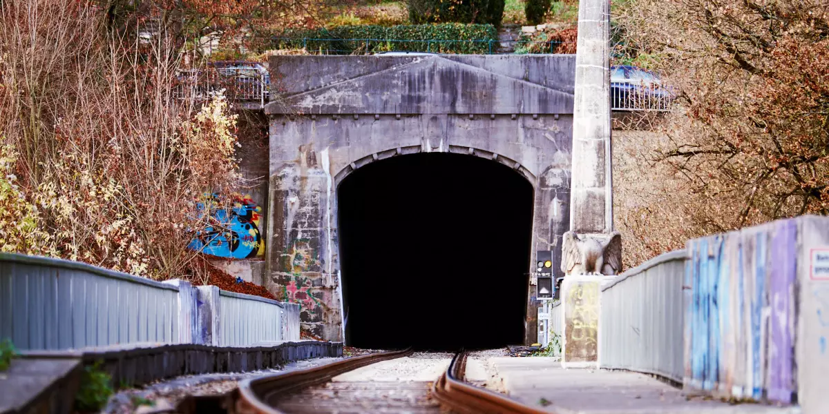 Froschperspektive mit Gleisen im Vordergrund, die in einen Eisenbahntunnel der Ammertalbahn in Tübingen führen.